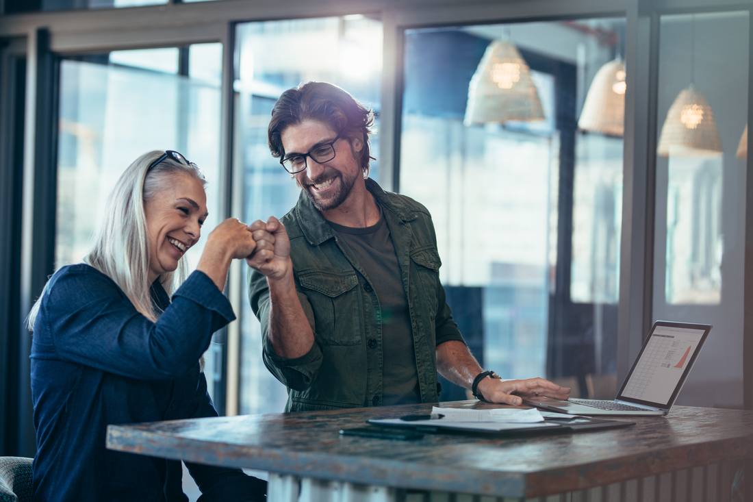 Two colleagues sharing a fist bump over a standing desk